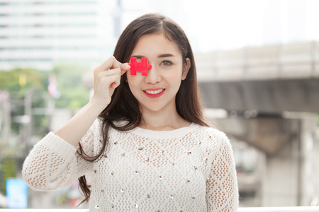 portrait of beautiful girl holding red jigsaw on streetの写真素材