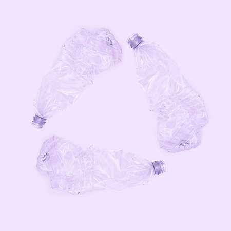 Three crashed plastic bottles on violet background form resycling sign. Plastic utilisation concept. Attractive ecological problem positive poster.の写真素材