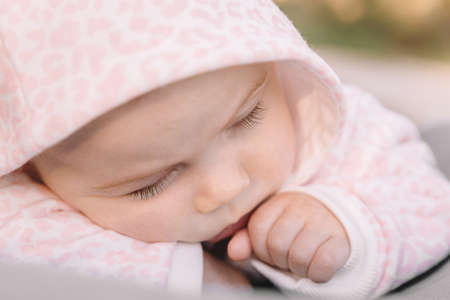 baby girl sleeping in a stroller in a pink jumpsuit in a hoodの写真素材