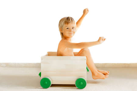 Blonde baby boy in a wooden box, with green wheels for toys, on a white background.の写真素材
