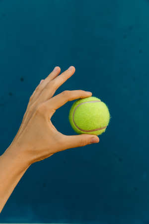 Yellow tennis ball in hand on the background of blue wall. Doing ok sign with hand and fingers. Successful expression.の写真素材
