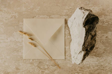 Craft envelope, blank greeting card, stone and wheat branch on a marble table. Flat lay, top view. Rustic autumn composition.の写真素材