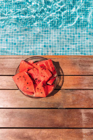 Round plate with watermelons near the pool on the plank floor. Summer concept.の写真素材