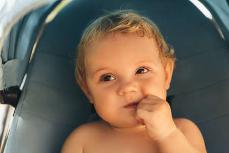 Beautiful baby girl in a blue stroller gnaws hand. 9 months old child.の写真素材