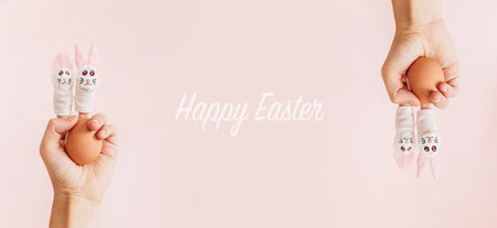 Easter egg in hand with toy bunnies on on fingers.. Minimal holiday concept. Easter poster and...