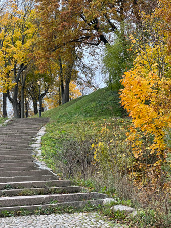 Beautiful autumn in city garden or park. A cobblestone road and a staircase with stone steps. Hills and ravines with trees and yellow leaves. Wonderful landscape.の写真素材