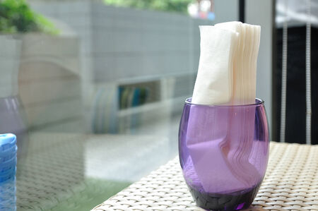 White tissues contained in violet glass on rattan table in food-shop.の写真素材