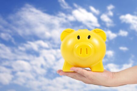 Man hand holding yellow piggy bank with blue sky