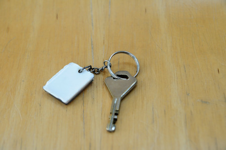 Single key with white key-chain on light wooden board