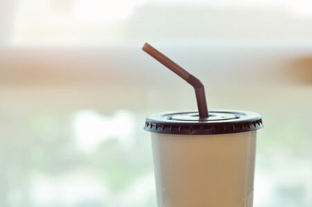 Beverage paper cup with straw next to windows with light flareの写真素材