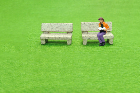 Selective focus miniature sitting on stone bench reading book, business concept.の写真素材