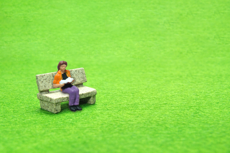Selective focus miniature sitting on stone bench reading book, business concept.の写真素材