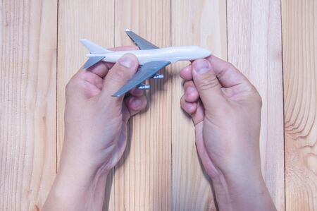 Man hand holding miniature of plastic airplane on wood table.の写真素材