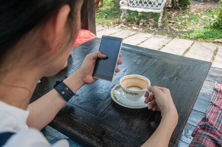 Unidentified people using smartphone and enjoy with hot coffee in fresh park.の写真素材