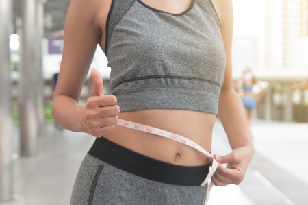 Young Asian woman slim body wearing sportwear use tape measure with her slender-waisted in middle of city.の写真素材