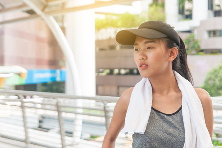 Young Asian woman has small white towel and gray hat posting show her slender body after exercise in middle city.の写真素材