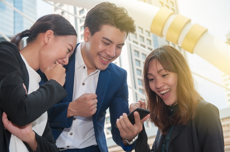 Asian young business man and business woman feel happy when project success. Business people checking text message by smart phone.の写真素材