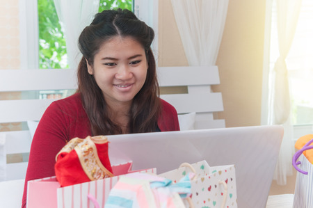 Asian pregnant woman wearing red cardigan using laptop and credit card for shopping online website on wooden table and many shopping bagの写真素材
