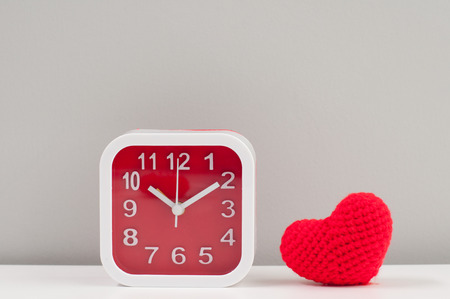 Time for love, square red and white frame alarm clock with knitting wool heart on white table and grey backgroundの写真素材