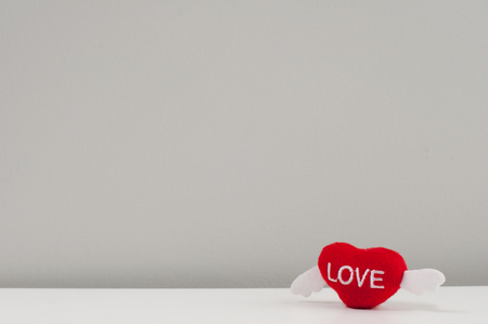 Red wool heart with white wings lay on white table with grey background, valentine love concept.の写真素材