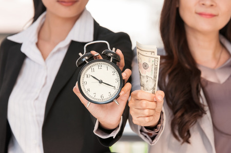 Asian businesswomen show black alarm clock and dollar bank note, business concept time to work be exchanged to money.の写真素材