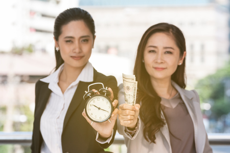 Young and middle Asian business people show dollar bank note and alarm clock, business concept time managing.の写真素材