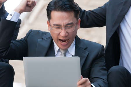 Middle Asian business man satisfy happy with their investment on his silver laptop with his friendの写真素材