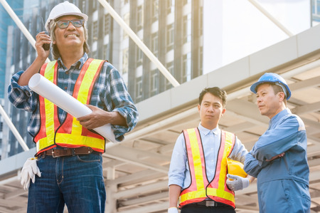 Asian civil engineer team wearing safety helmet and uniform using blueprint to meeting, discussing...