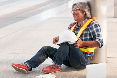 Happy middle Asian civil engineer sitting for rest and hold white safety helmet on left hand with laptop.の写真素材