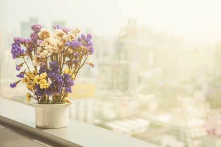 Vintage dry flowers in ceramic flower pot lay on next to high building window with blur city town background.の写真素材