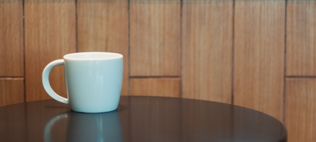 White middle coffee cup lay on black table and wooden wall.の写真素材