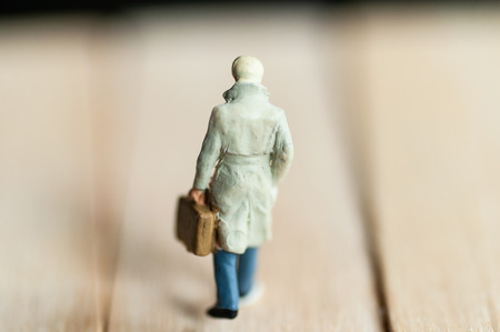 Selective focus miniature business people   walking and holding brown briefcase on wooden floor.