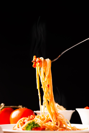 Hot spaghetti with tomato sauce in white plate,  food stylish action with black background, pull spaghetti up with fork.の写真素材