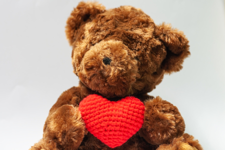 Cute dark brown bear holding wool red heart sitting on gray background, give love valentine lover concept.の写真素材