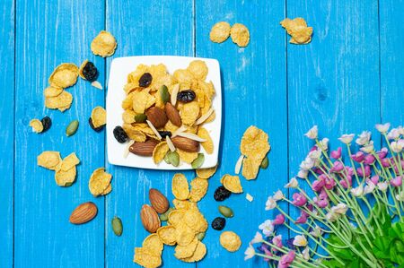 Cornflakes mix with almond rasin sunflower seeds on blue wooden plank.  Breakfast for children...