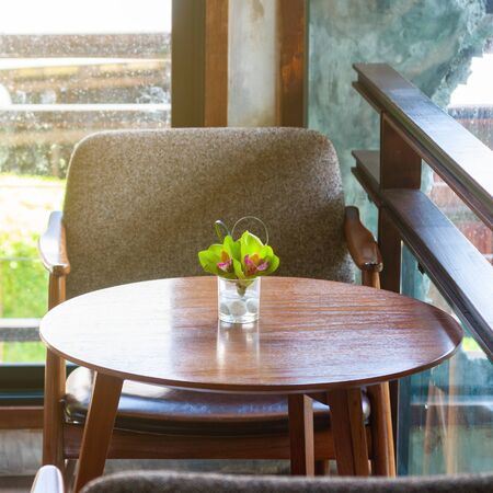 House decoration, flower in glass on wooden table with arm chair.  coffee table with flowers.