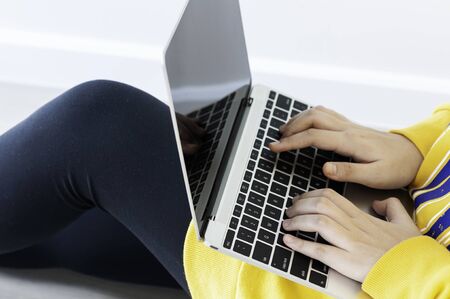Coronavirus crisis, Asian female teenager use 18 years old do online learning from home by laptop, woman wearing casual yellow cloth use laptop for work from home during corona virus crisis. Thailand.の写真素材