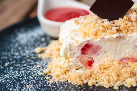 Strawberry cheesecake with crispy crumble and piece of chocolate plate and icing with strawberry sauce and vanilla sauce serve on classic black plate.の写真素材