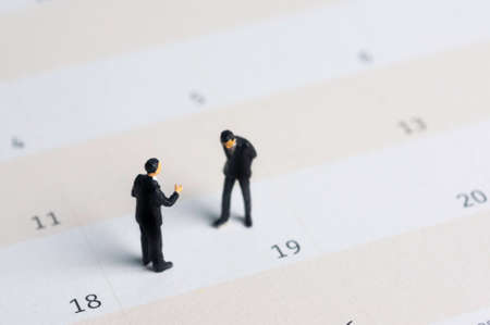 Selective focus miniature businessman standing on calendar checking schedule.の写真素材