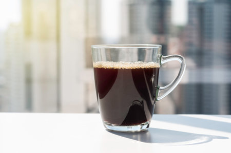 Glass of Americano black coffee refreshment next to high building window with hard light and shadow....