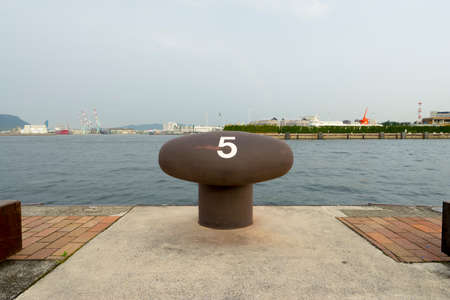 Big metal stake for ferry on port, sea and gray sky on background.の写真素材