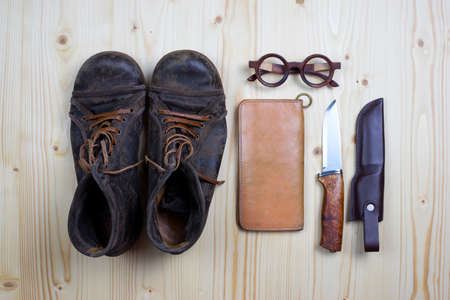 Top view brown leather vintage menâs boots, wallet, knife and wooden glasses on flat pine wood.の写真素材