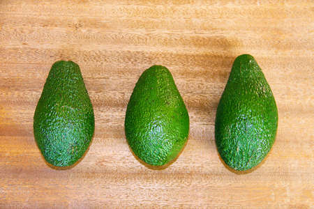 Three green avocados on a wooden background.