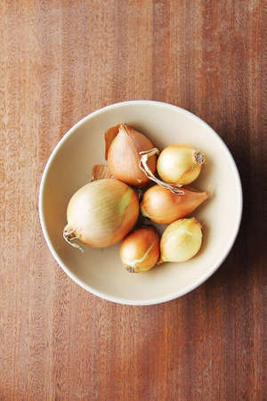 Six yellow onion heads in a deep ceramic plate bezhegogo colors on a wooden board.の写真素材