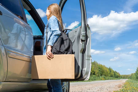 A young girl, a teenager with a backpack, hitchhiking stopped the car for a trip, talking to the driver about the trip, holding a sign with a place for the text in her hands. Travel concept, passing car, vacation. High quality photoの写真素材