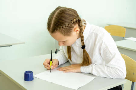 A cute schoolgirl kid sitting at a school desk and writes in her notebook. Back to school education...
