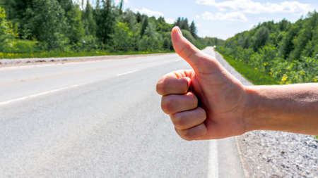 Hitchhikers give a thumbs up on the background of the road on a summer day in close-up. The concept...