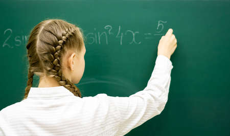 Female student teenager at a math lesson writing in chalk on a blackboard. Education, adolescence,...