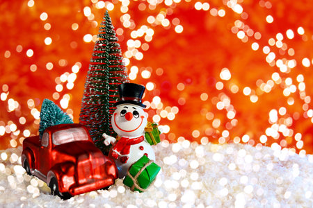 On a red background with bokeh, a cheerful snowman near a pickup truck with a Christmas tree. Christmas banner, card with place for text.の写真素材