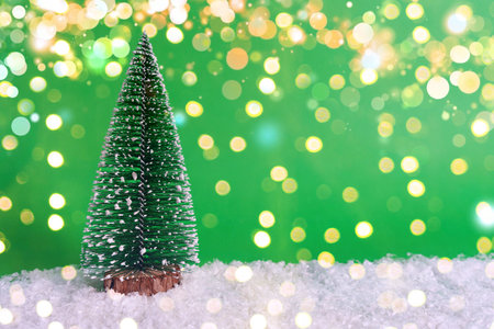 Snow-covered Christmas tree on snow and green background with bokeh. Christmas banner concept, card with mark for copy.の写真素材